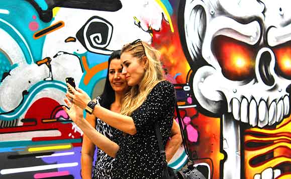 Participantes da festa Chilli Beans na Rua faz selfy diante de arte de rua  criada no local da festa